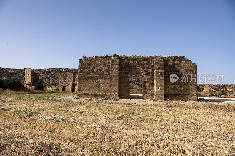 Agios Mamas教堂，背景是废弃的废墟，前景是收获的农田，在蓝天下